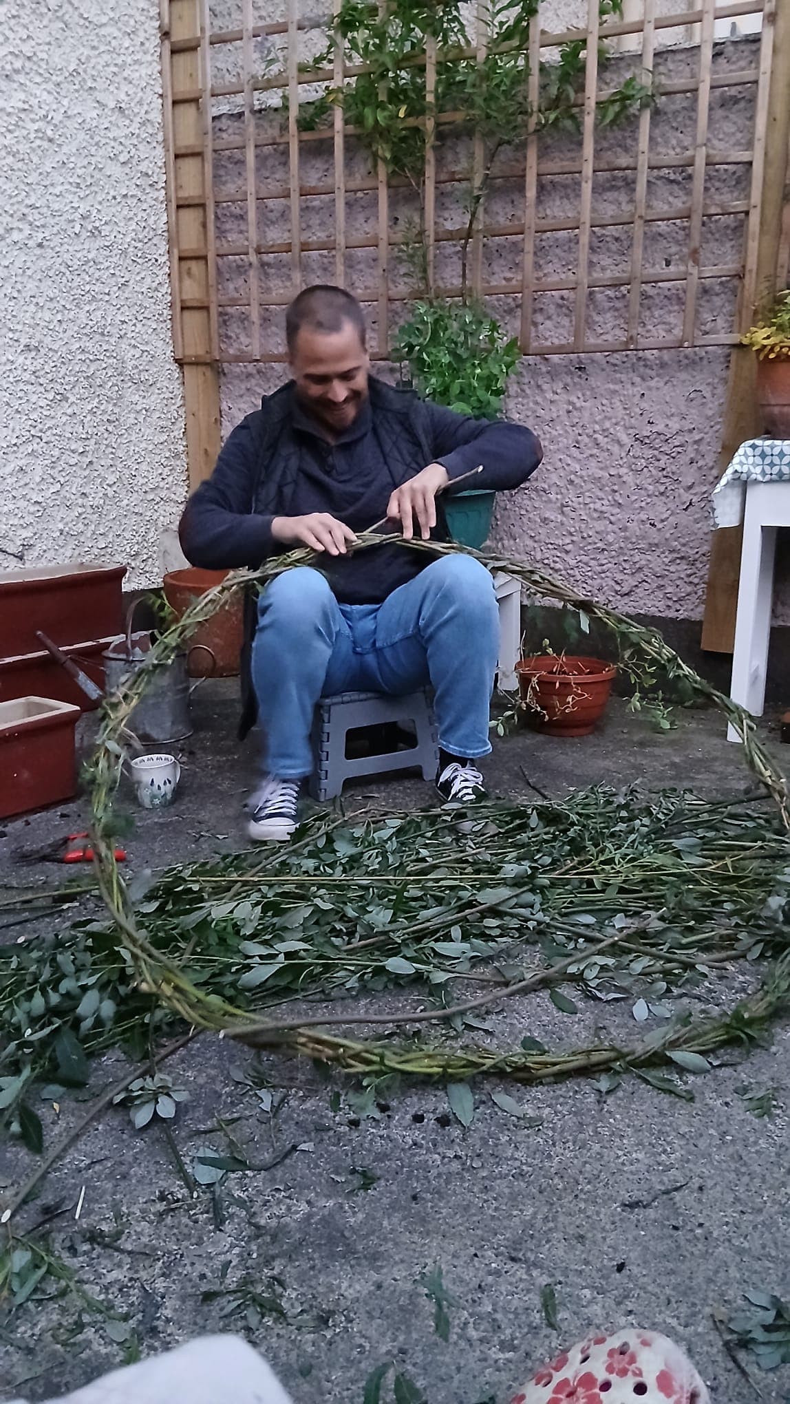 Russell seated on a stool, weaving willow branches into a traditional salley belt