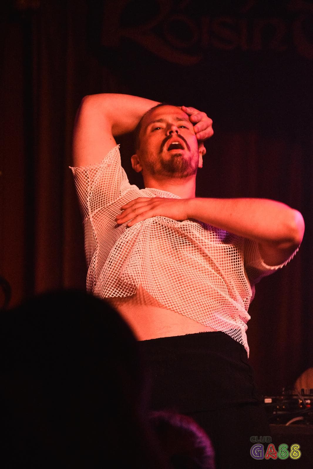 Russell, a man with short dark hair dancing on a nightclub stage in a moment of sensuality while his hands run aroudn his head and chest