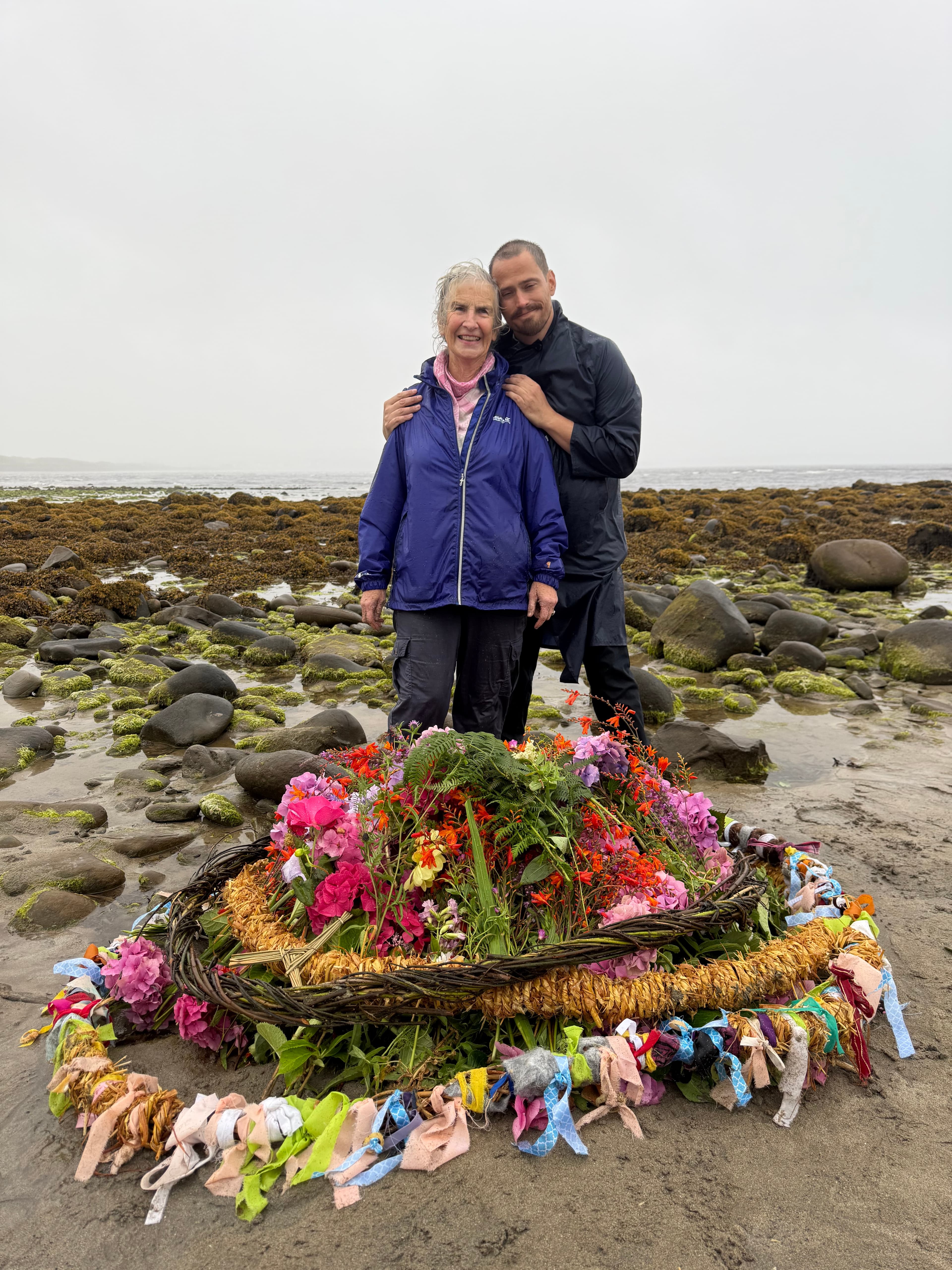 Returning to Kilmacreehy Strand but this time with multiple salley belts laid on the beach with a mound of flowers inside while Russell leans tenderly with his eyes closed with Daire, who was in the first picture teaching him how to strip and weave sallies
