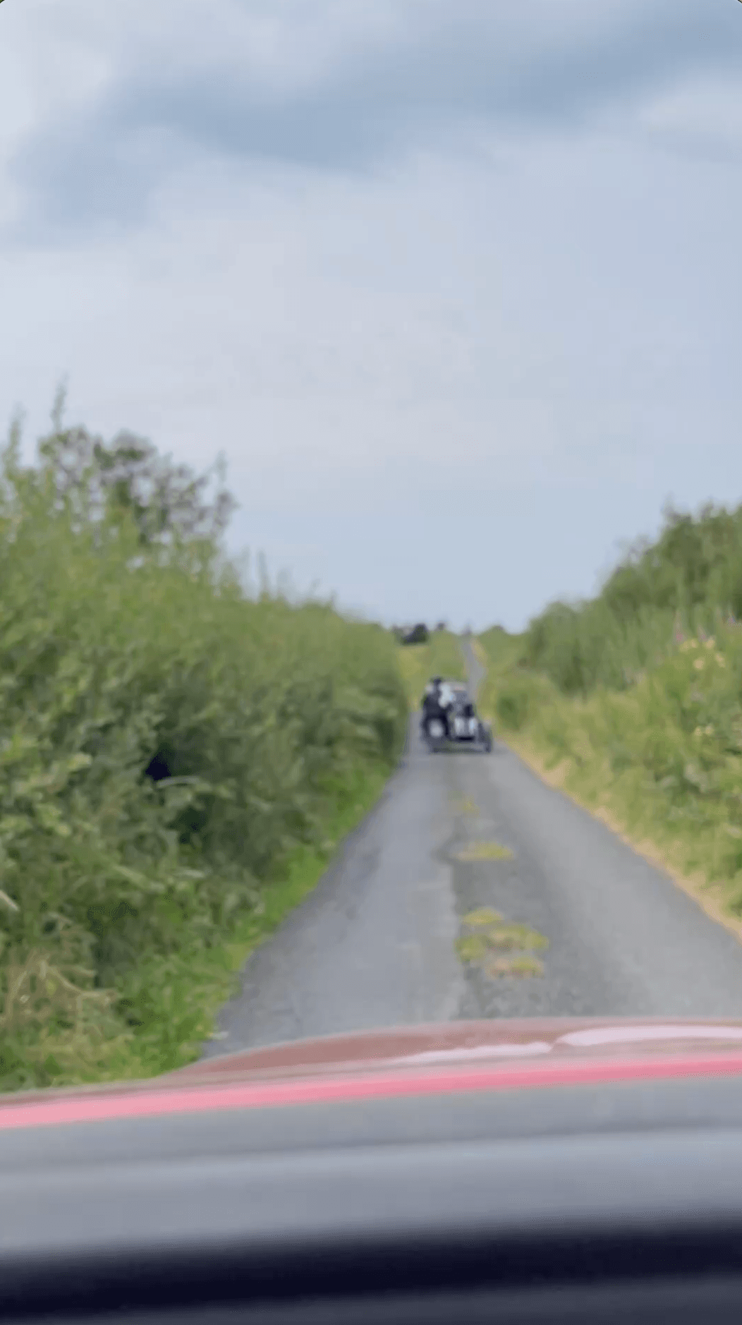 A dashboard photograph of an Irish road in Clare with motorcycle and sidecar blurred in the distance ahead while sallies (willows) line the road